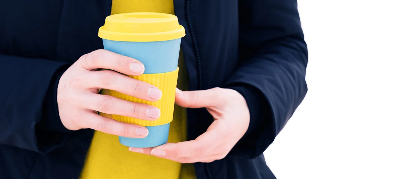 Mensch hält einen wiederverwendbaren To-Go-Becher in den Händen