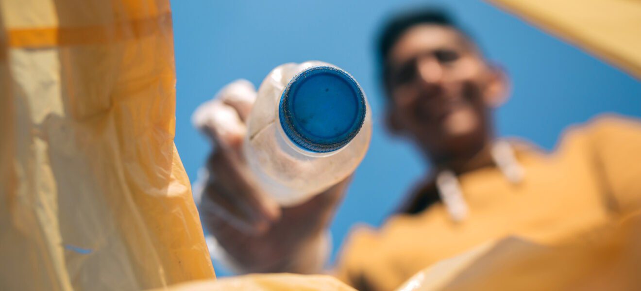 Mann hält Plastikflasche in die Gelbe Tonne