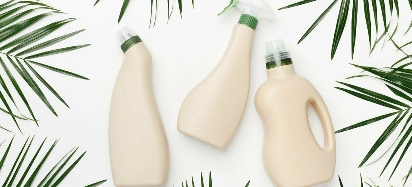 Drei Flaschen aus Bioplastik vor weißem Hintergrund umrahmt mit Palmblättern