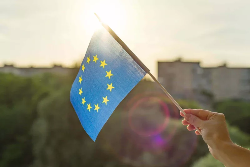 Hand schwenkt Europaflagge vor grünem Hintergrund