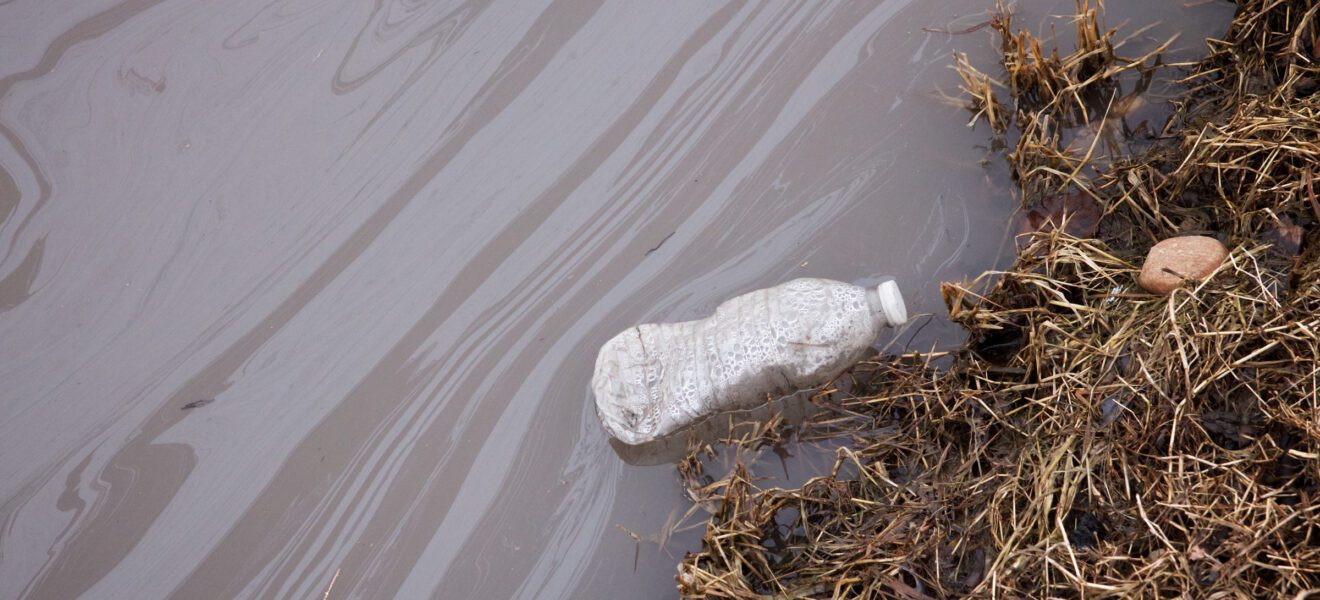 PFAS belastete Flasche treibt im schmutzigen Wasser