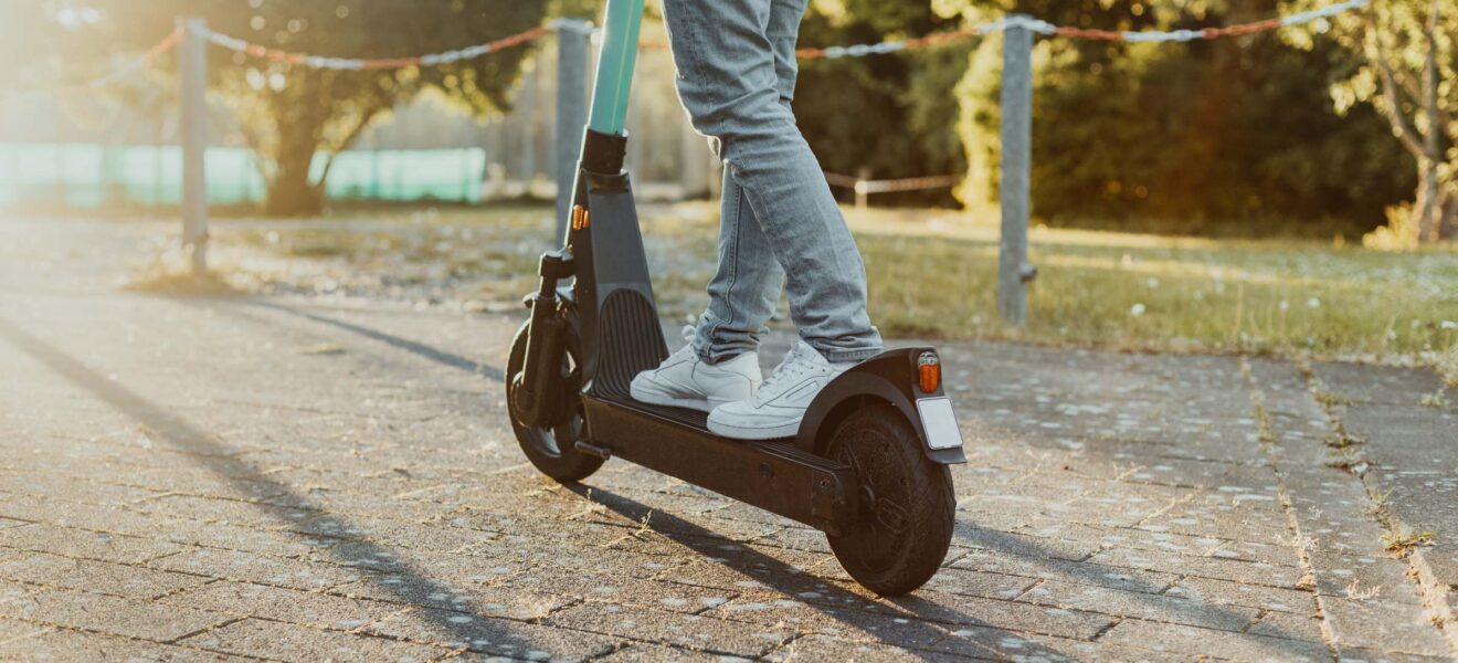 Person fährt mit einem E-Scooter auf einem sonnigen Weg in der Stadt