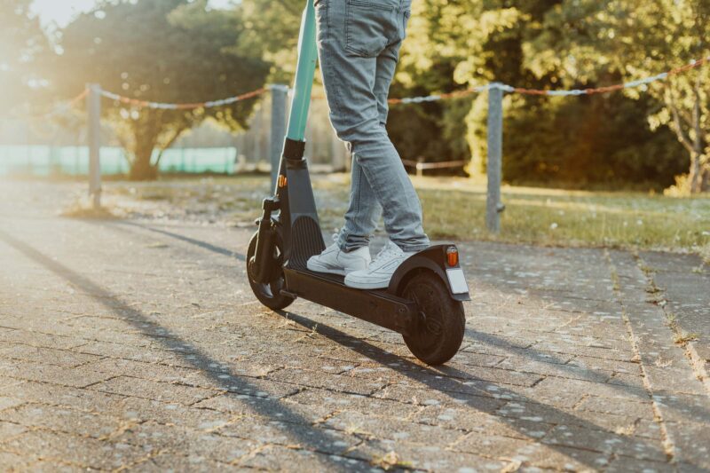 Person fährt mit einem E-Scooter auf einem sonnigen Weg in der Stadt