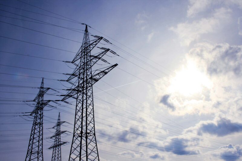 Hochspannungsleitungen und Strommasten unter blauem Himmel mit Sonne