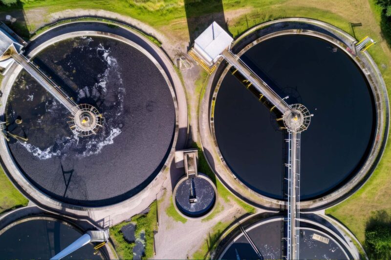 Das Bild zeigt eine Luftaufnahme mehrerer kreisförmiger Abwasserbehandlungstanks, die in der Dämmerung in Betrieb sind.