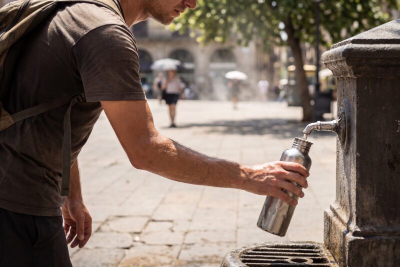 Mann füllt Wasserflasche an Trinkbrunnen in der Stadt auf.