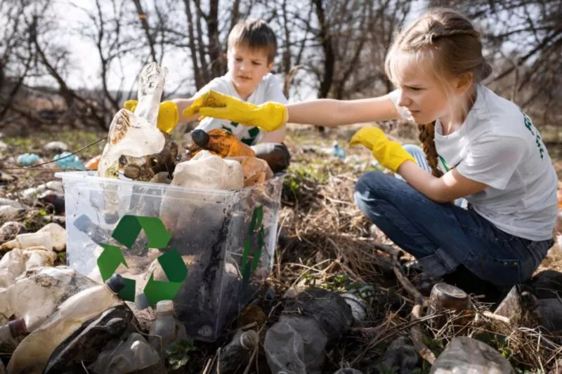 Kinder sammeln Plastikmüll im Wald zur Wiederverwertung und Umweltschutzaktion