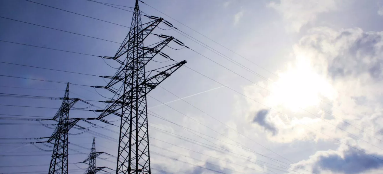 Hochspannungsleitungen und Strommasten unter blauem Himmel mit Sonne