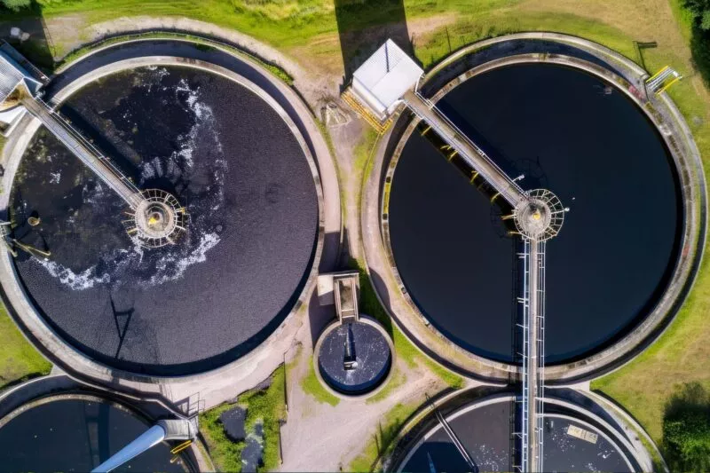 Das Bild zeigt eine Luftaufnahme mehrerer kreisförmiger Abwasserbehandlungstanks, die in der Dämmerung in Betrieb sind.