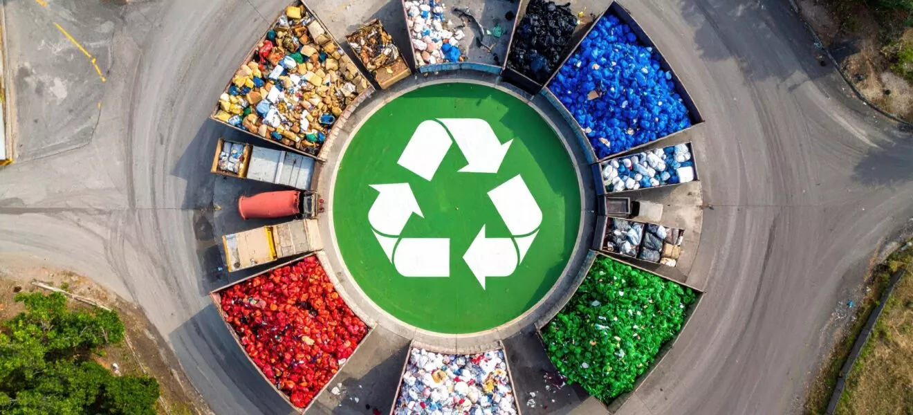 Luftaufnahme von Recyclingbehältern in lebendigen Farben, die einen Kreis um ein grünes Recyclingsymbol bilden und Nachhaltigkeit fördern.